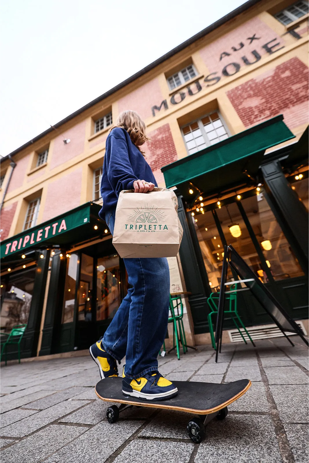 Jeune skateur devant une pizzeria Rue Forno avec une pizza à emporter.