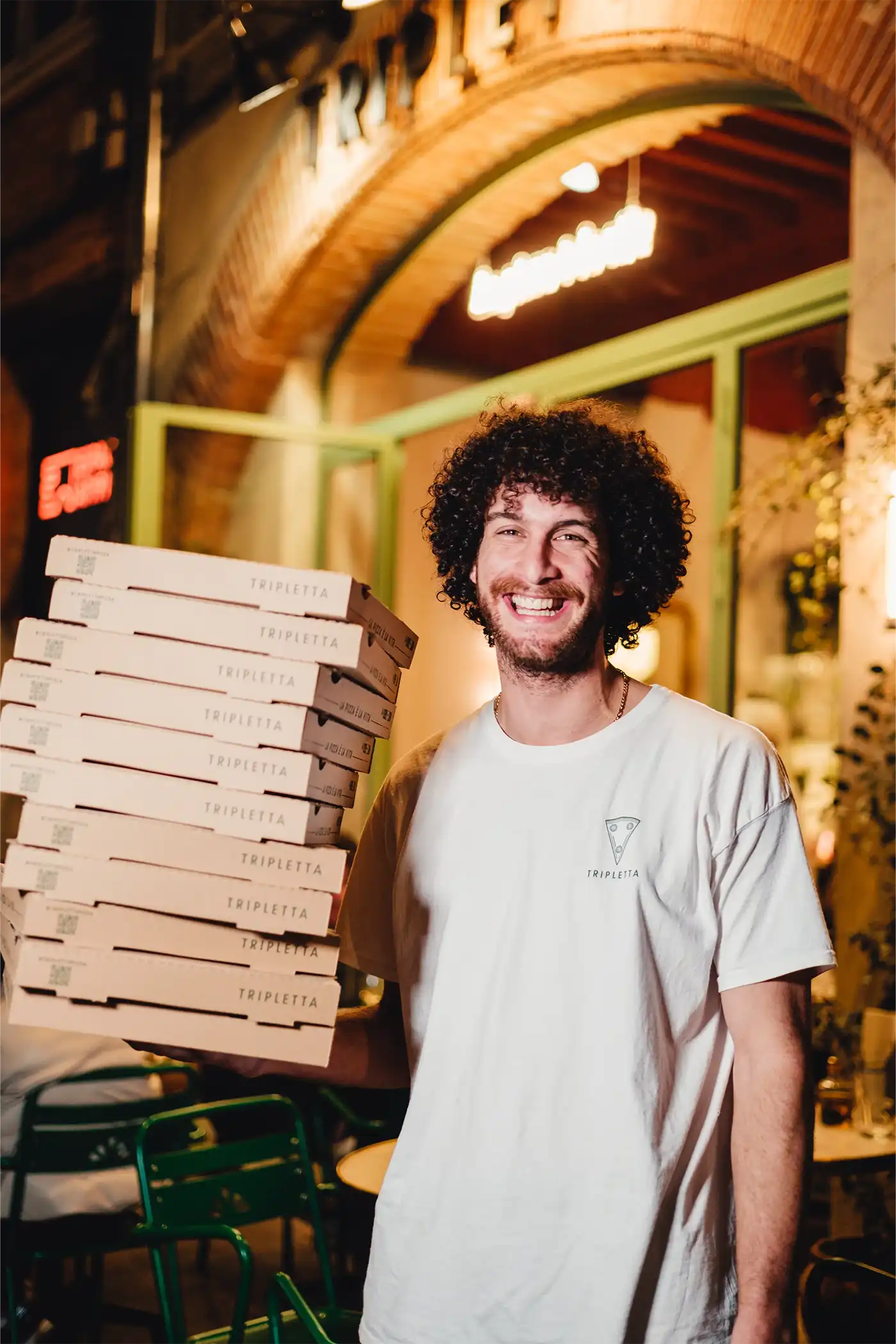 Jeune homme souriant, portant une pile de boîtes de pizza Rue Forno.