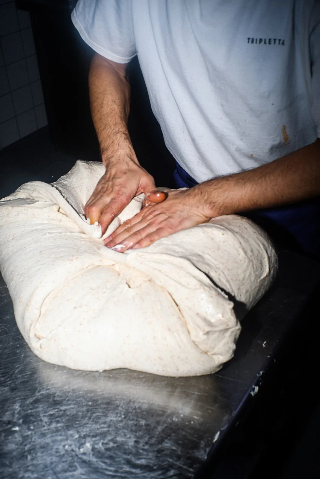 Pâton de pizza en cours de pétrissage à la main par un cuisinier Rue Forno.